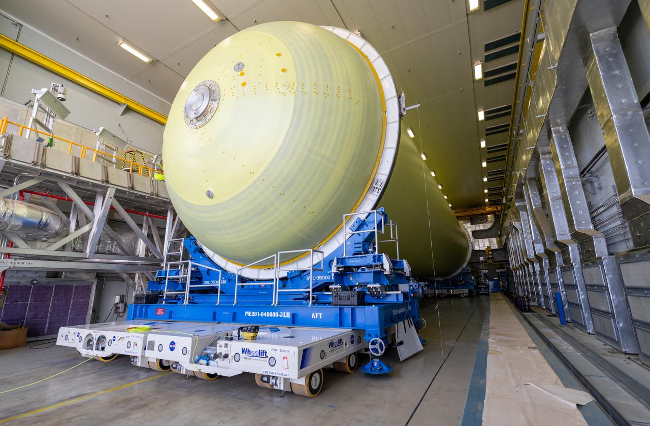 Teams move a liquid hydrogen tank for NASA’s SLS (Space Launch System) rocket out of a priming cell and into an adjacent cell on May 20 at the agency’s Michoud Assembly Facility in New Orleans. Inside the cell, the tank, which will be used on the core stage of NASA’s Artemis III mission, will receive its thermal protection system.  The thermal protection system, or spray-on foam insulation, provides protection to the core stage during launch. It is flexible enough to move with the rocket yet can withstand the aerodynamic pressures as the SLS accelerates from 0 to 17,500 mph and soars to more than 100 miles above the Earth. This third-generation insulation is more environmentally friendly and keeps the cryogenic propellant, which powers the rocket’s four RS-25 engines, extremely cold (the liquid hydrogen must remain at minus 423 degrees Fahrenheit/253 degrees Celsius) to remain in its liquid state. When applied the thermal protection system is a light-yellow color, which “tans” once exposed to the Sun’s ultraviolet rays, giving the SLS core stage its signature orange color.
